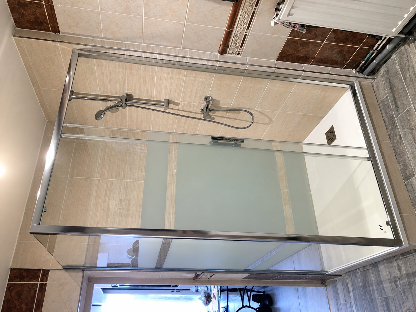 Une cabine de douche à cadre chromé et parois en verre avec bandeau dépoli, installée dans une salle de bain carrelée, photographiée de côté.